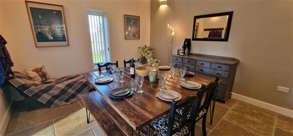 dining area with large square wooden table with 4 chairs and 2 matching wooden benches, a chaise bench in the corner, a chest of drawers with a large mirror over